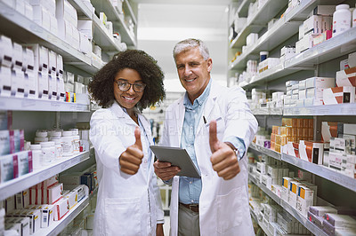 Buy stock photo Portrait of two cheerful pharmacists holding a digital tablet and showing thumbs up while looking at the camera