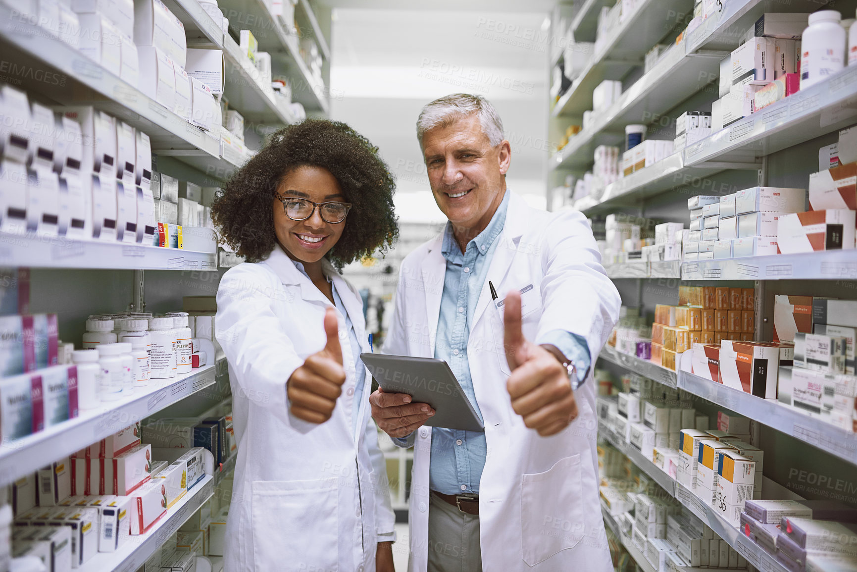 Buy stock photo Portrait of two cheerful pharmacists holding a digital tablet and showing thumbs up while looking at the camera