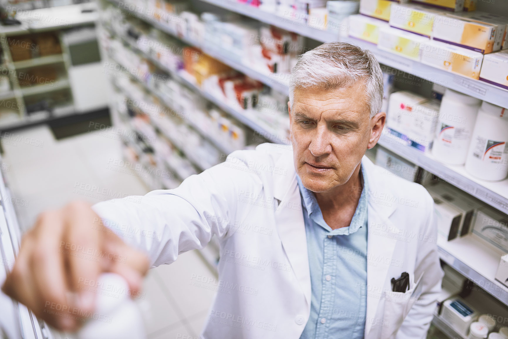 Buy stock photo Shot of a focused mature male pharmacist putting a medication bottle back on the shelf in a pharmacy