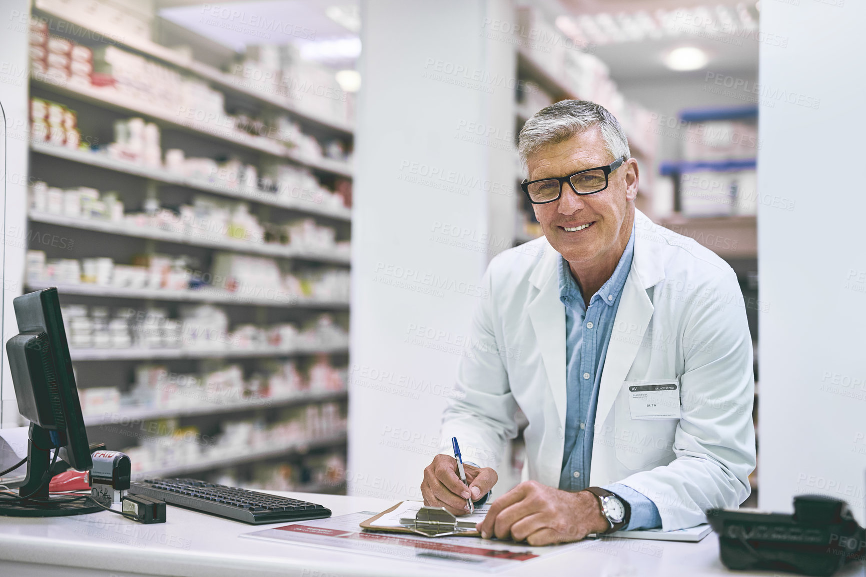 Buy stock photo Portrait of a confident mature male pharmacist making notes in a book on the counter while looking at the camera