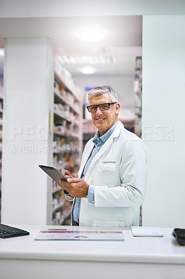 Buy stock photo Portrait of a confident mature male pharmacist making notes on a tablet while looking at the camera in a pharmacy