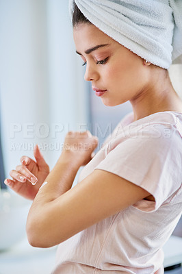 Buy stock photo Cropped shot of a beautiful young woman applying moisturizer to her skin in the bathroom at home