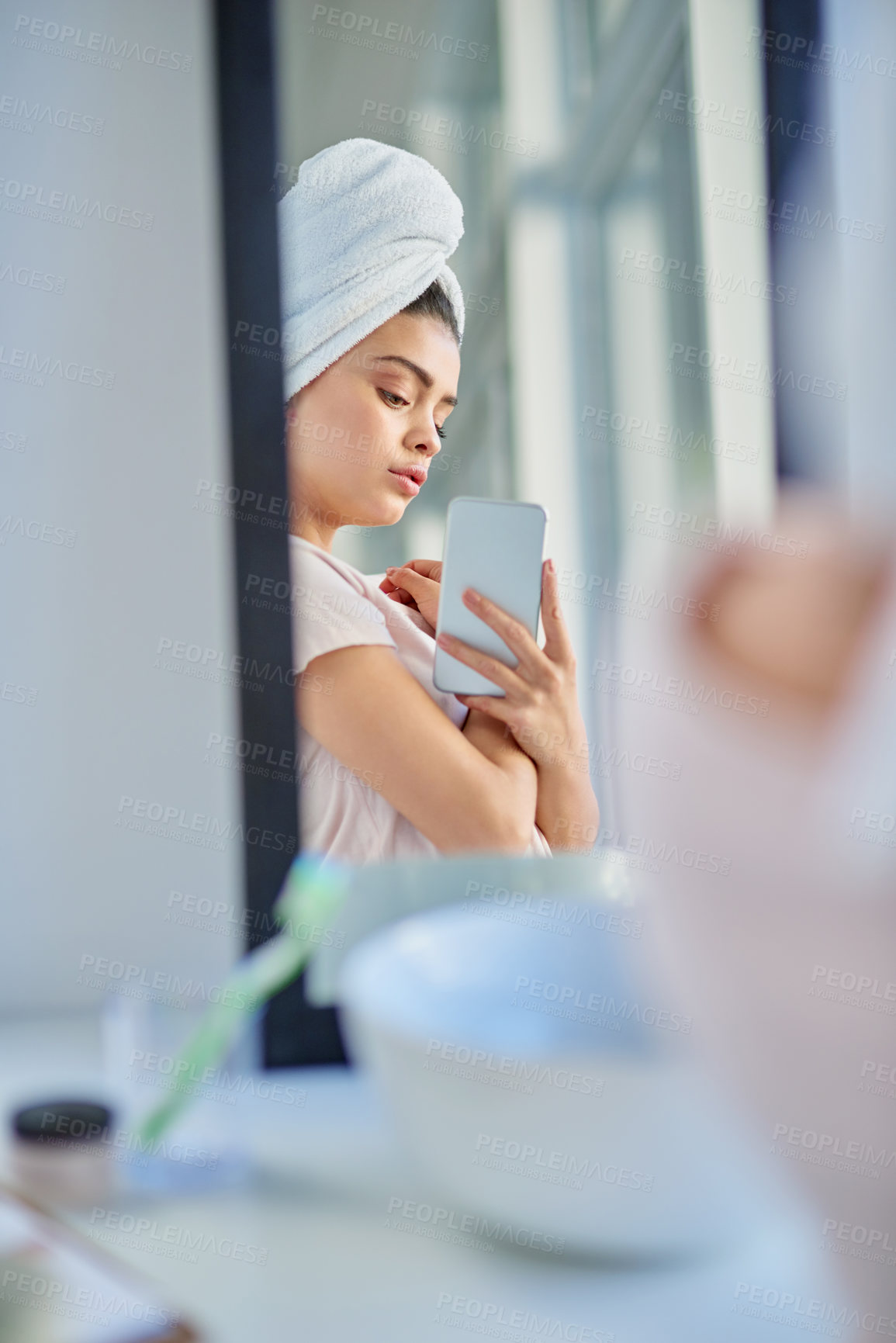 Buy stock photo Cropped shot of a beautiful young woman using her cellphone to check her skin in the bathroom at home