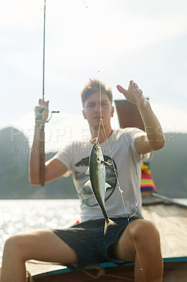 Buy stock photo Cropped shot of a handsome young man fishing while out at sea on his boat