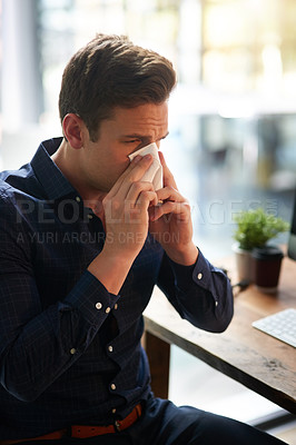 Buy stock photo Shot of a young businessman blowing his nose in an office
