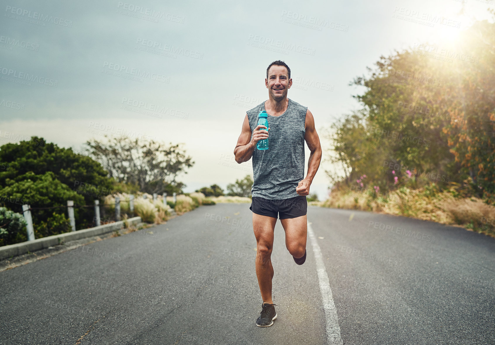 Buy stock photo Running, happy man and portrait with water bottle for exercise, cardio and fitness on road in nature. Male athlete, smile and workout on trail for health, sport or marathon training with sportswear