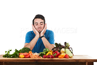 Buy stock photo Studio shot of a young man looking disinterested while posing with a variety of fresh vegetables against a white background