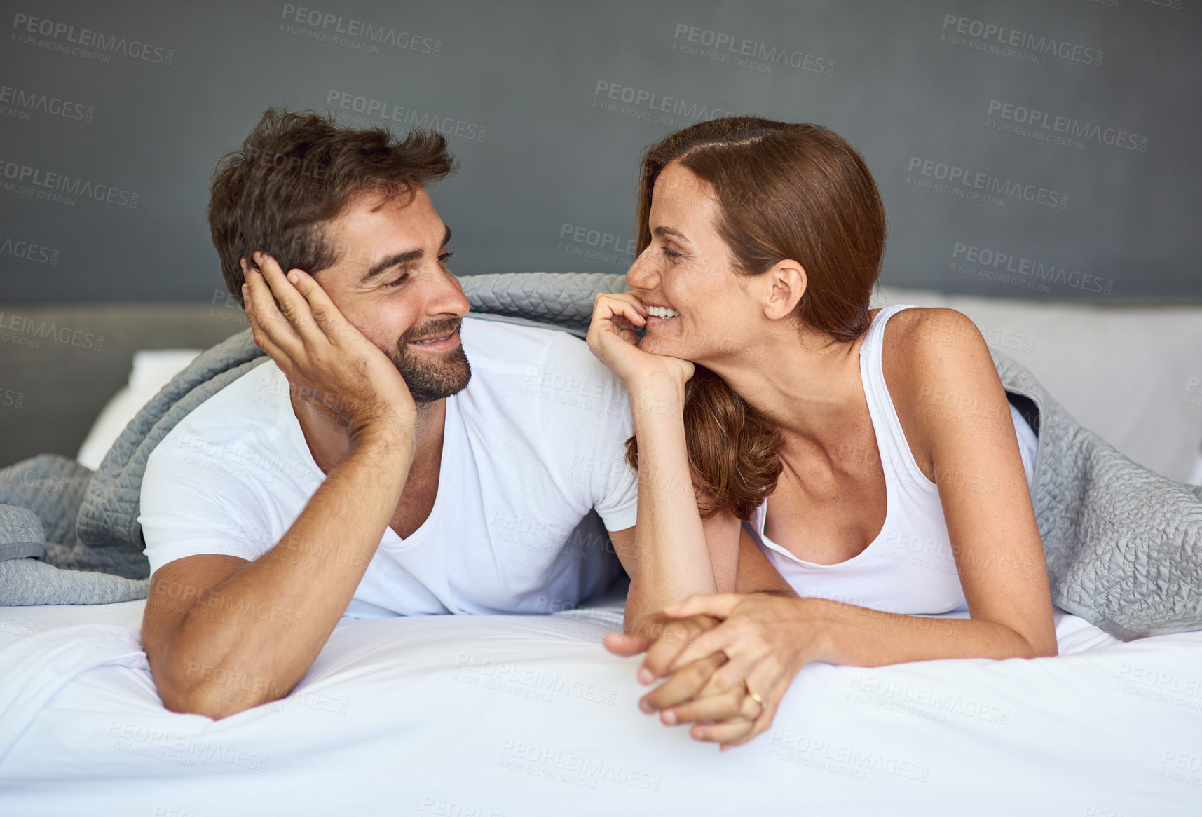 Buy stock photo Happy couple, relax or holding hands on bed in morning, peace or love for marriage commitment at house. Blanket, woman or man with smile for romantic relationship, bonding or anniversary together