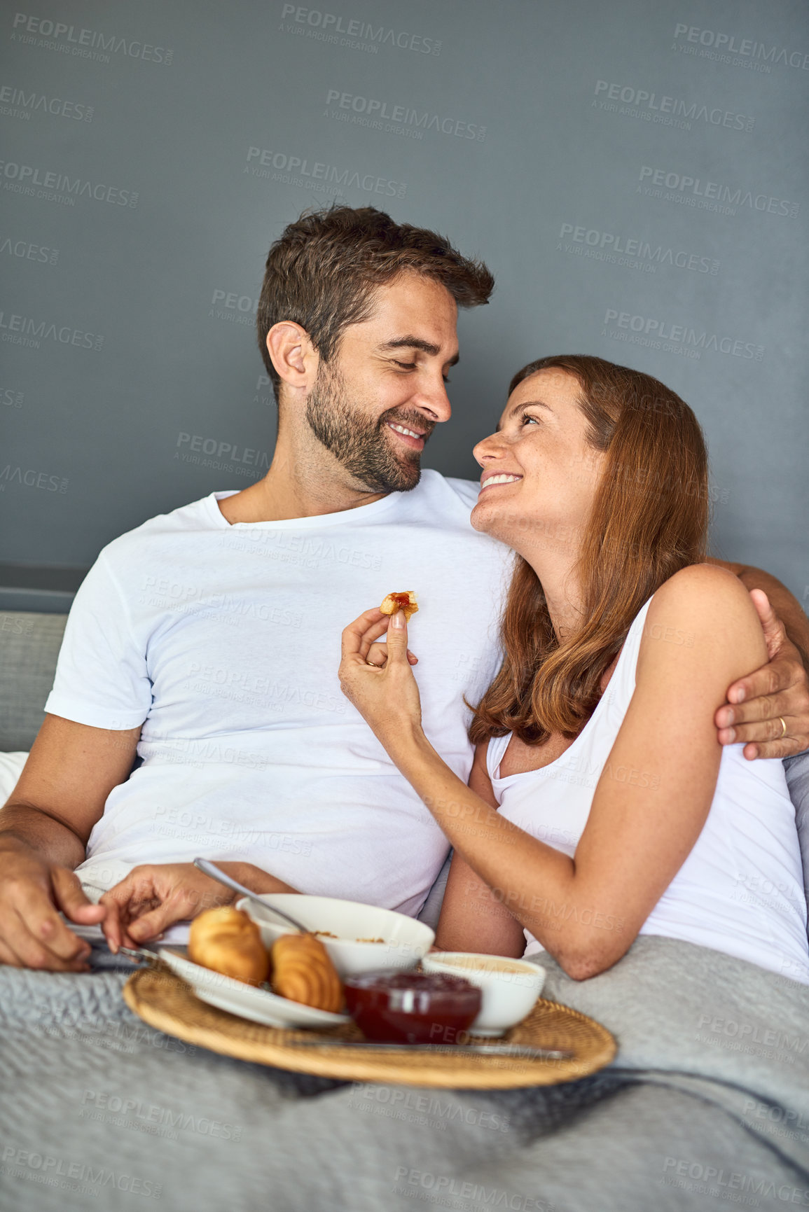 Buy stock photo Couple, eating and happy in bed for breakfast at hotel with room service for love and valentines day. Man, woman and smile in morning in bedroom for support, food and celebration together on vacation