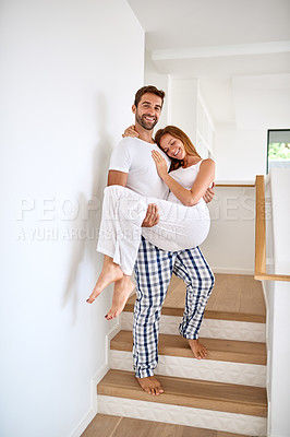 Buy stock photo Shot of a young man lovingly carrying his wife down the stairs at home