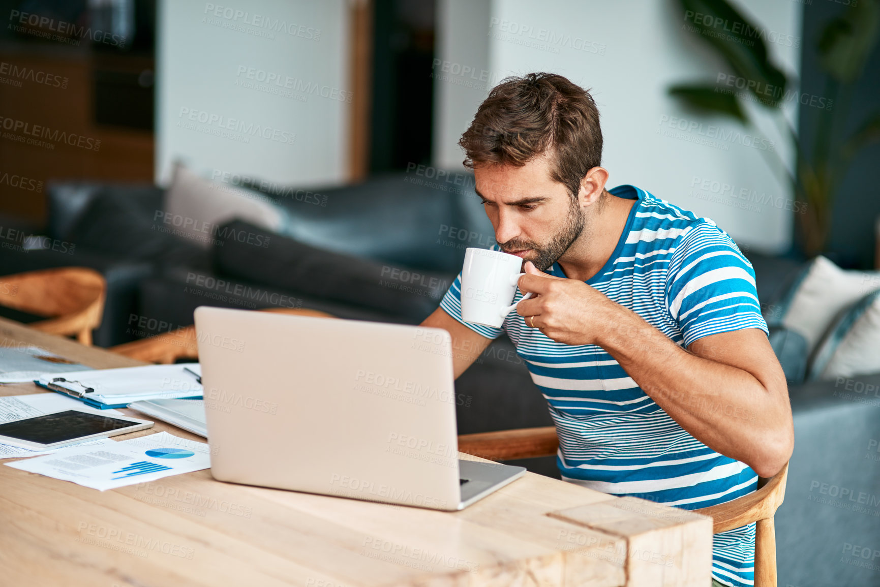 Buy stock photo Cropped shot of a handsome young male entrepreneur drinking coffee while working from his home office