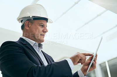 Buy stock photo Shot of a focused professional male architect standing next to a development site while using a digital tablet inside of a building