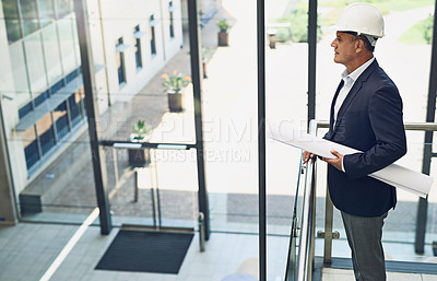 Buy stock photo Shot of a focused professional male architect looking at a development site while holding blueprints inside a building