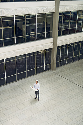 Buy stock photo High angle shot of a cheerful professional male architect holding blueprints while looking up inside of a building