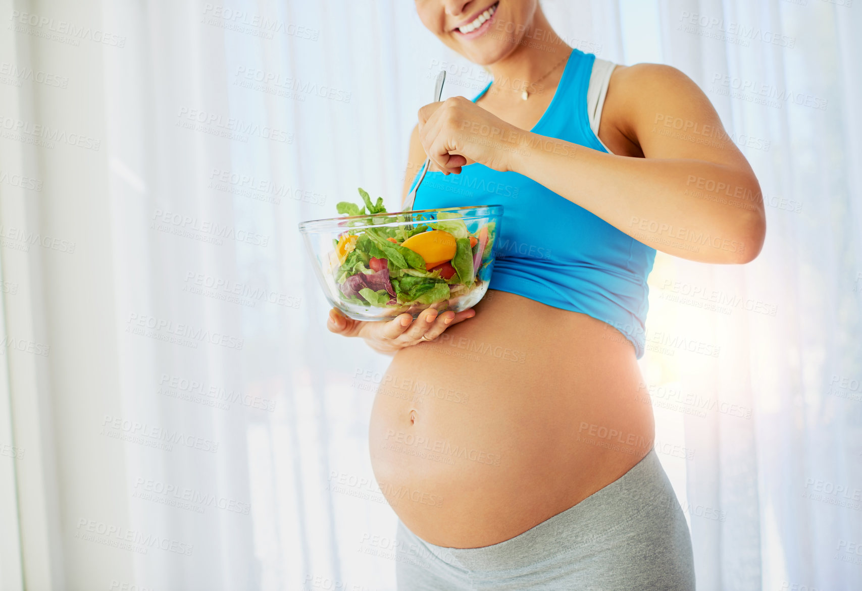 Buy stock photo Shot of a fit pregnant woman eating a bowl of salad at home