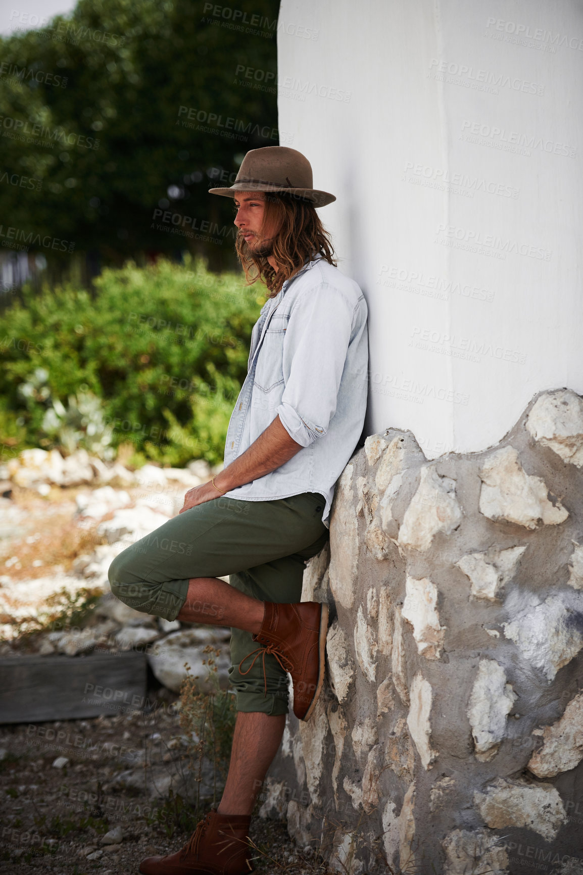 Buy stock photo Shot of a trendy young man leaning against the wall of a building outside