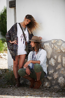 Buy stock photo Shot of a trendy young couple standing together against the wall of a building outside