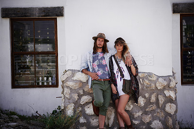 Buy stock photo Shot of a trendy young couple standing together against the wall of a building outside