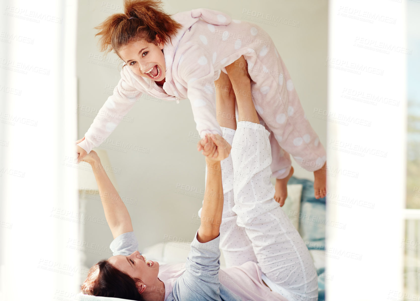 Buy stock photo Shot of a young mother lifting her daughter with her legs while lying on bed