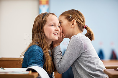 Buy stock photo Shot of an elementary school girl whispering in her friend's ear in class