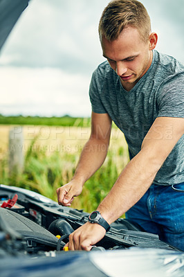 Buy stock photo Shot of a young man checking under the hood of his car after breaking down on the road