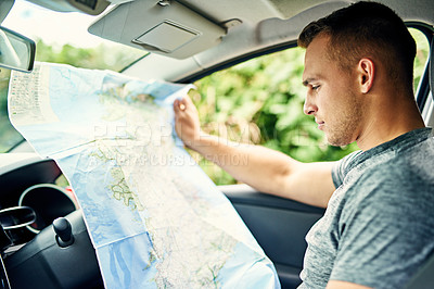 Buy stock photo Shot of a young man reading a map while traveling in a car