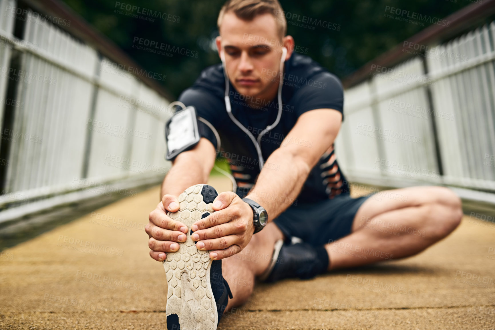 Buy stock photo Shot of a sporty young man stretching before a run outdoors