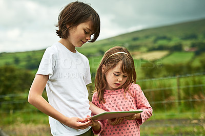 Buy stock photo Shot of two little siblings using a digital tablet together outdoors