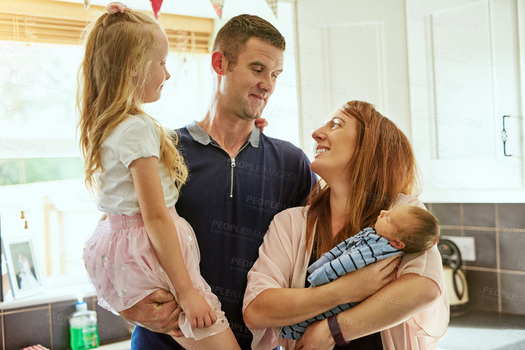 Buy stock photo Shot of a cheerful young family grouped together while standing inside the kitchen at home