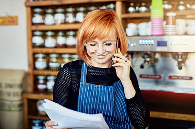 Buy stock photo Shot of a shop owner talking on her cellphone while looking at paperwork