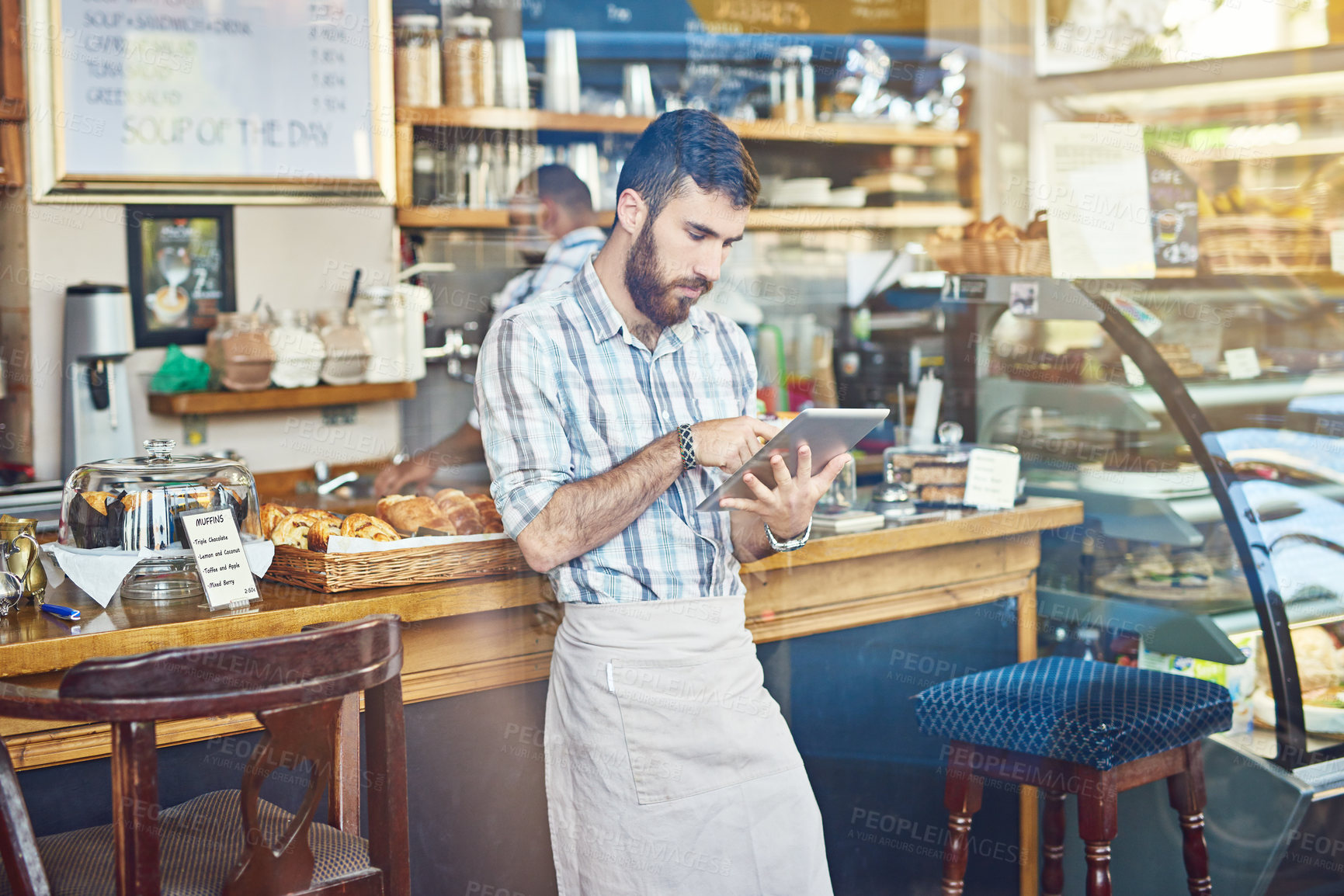 Buy stock photo Shot of a young man using a digital tablet while working in a coffee shop