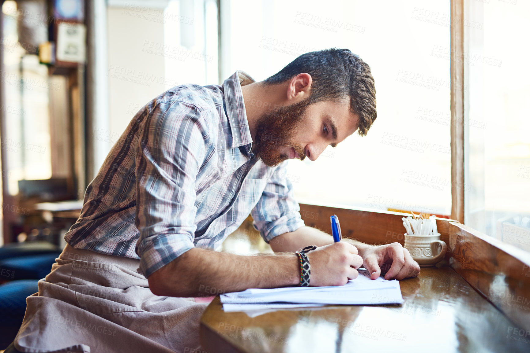 Buy stock photo Coffee shop, writing and man with documents by window for inventory, menu items and stock checklist. Restaurant, small business and person with paperwork for planning, budget review and cafe products