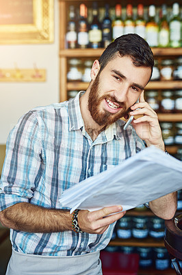 Buy stock photo Shot of a shop owner talking on his cellphone while looking at paperwork