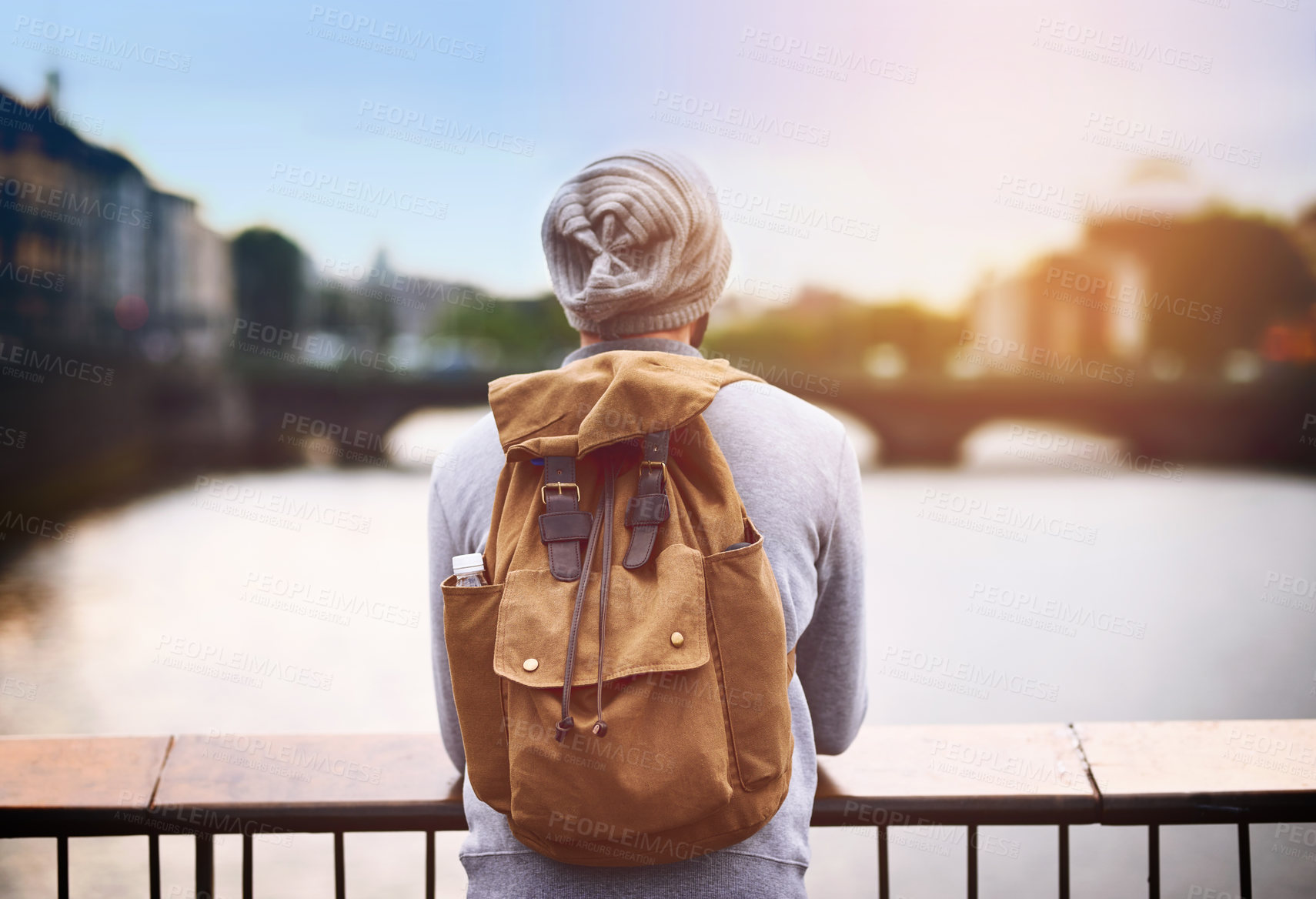 Buy stock photo Back, travel and a tourist man by a lake in the city for adventure or a journey of self discovery abroad. Bridge, view and blurred background with a male traveler standing outside in an urban town