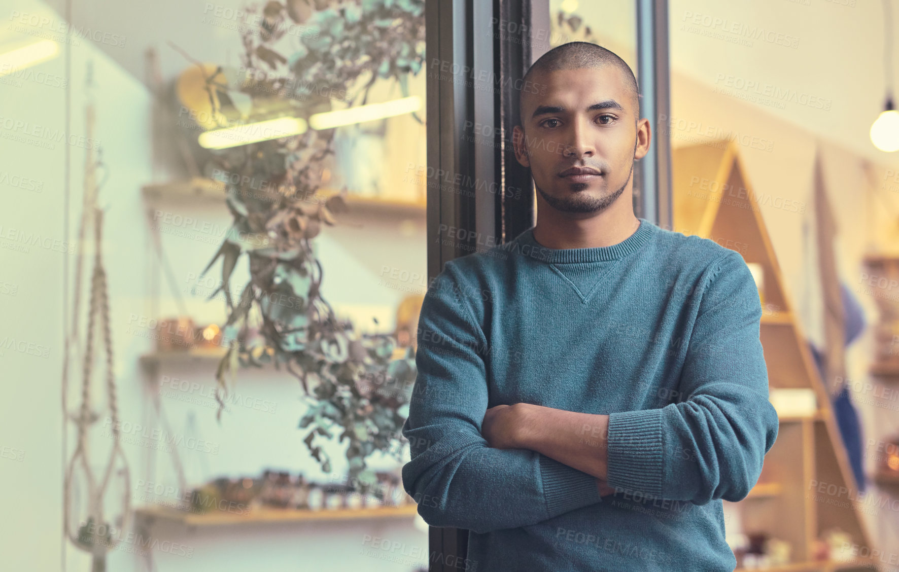 Buy stock photo Cropped portrait of a handsome young male entrepreneur standing with his arms folded in his store