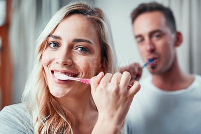 Buy stock photo Portrait of a young couple brushing their teeth together in the bathroom at home