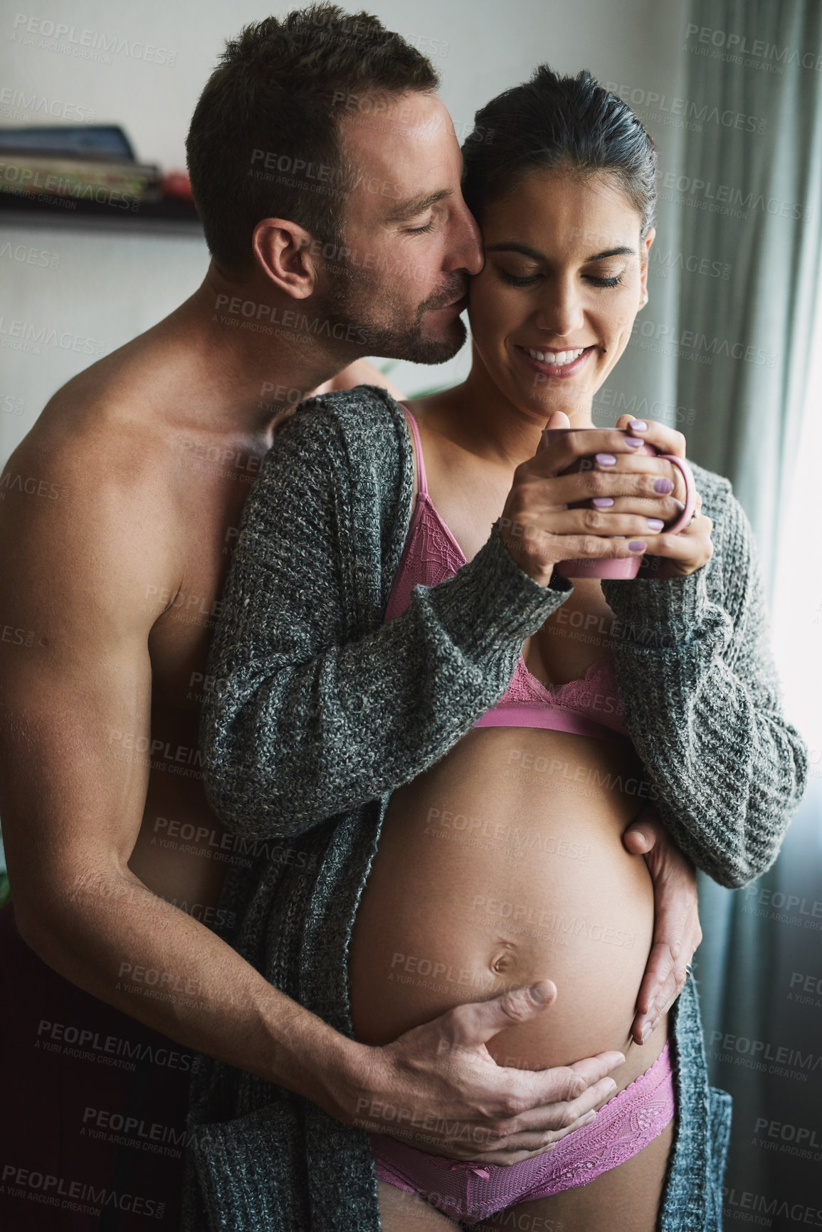 Buy stock photo Pregnancy, couple and kiss in home for love, touch and herbal tea for antioxidants. Future parents, happy and woman in underwear for growth, maternity or drink for healing with hug belly for bonding