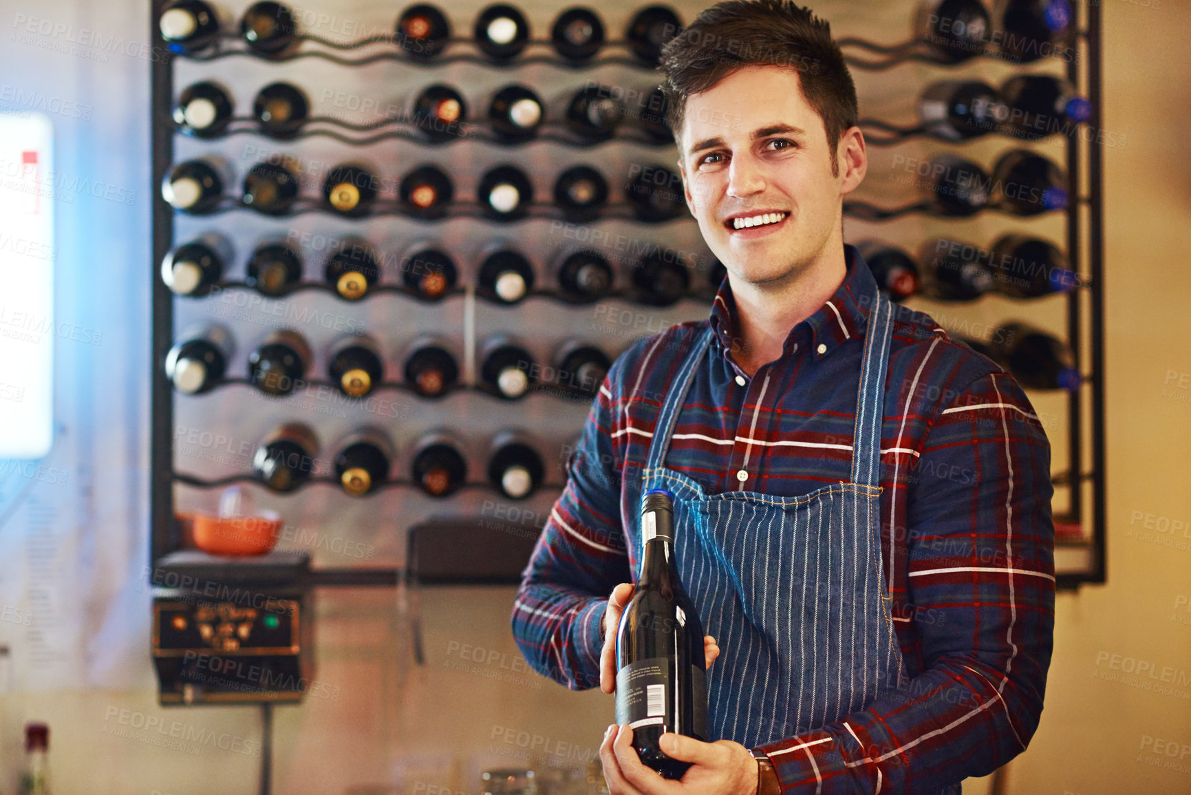 Buy stock photo Shot of a handsome young man choosing a bottle of wine in a restaurant