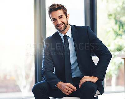 Buy stock photo Shot of a handsome young businessman sitting on a chair in a modern office
