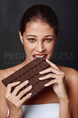 Buy stock photo Cocoa, portrait and woman in studio eating for unhealthy diet, craving sugar or cheat day on dark background. Bite, face and female model for snack temptation, sweet addiction or chocolate bar
