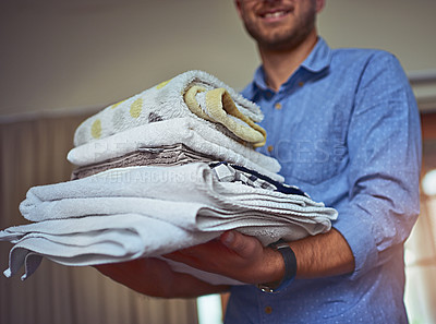 Buy stock photo Cropped shot of a young man holding a load of freshly folded clean laundry