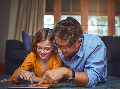 Buy stock photo Shot of a father and daughter lying on the floor and using a digital tablet together at home