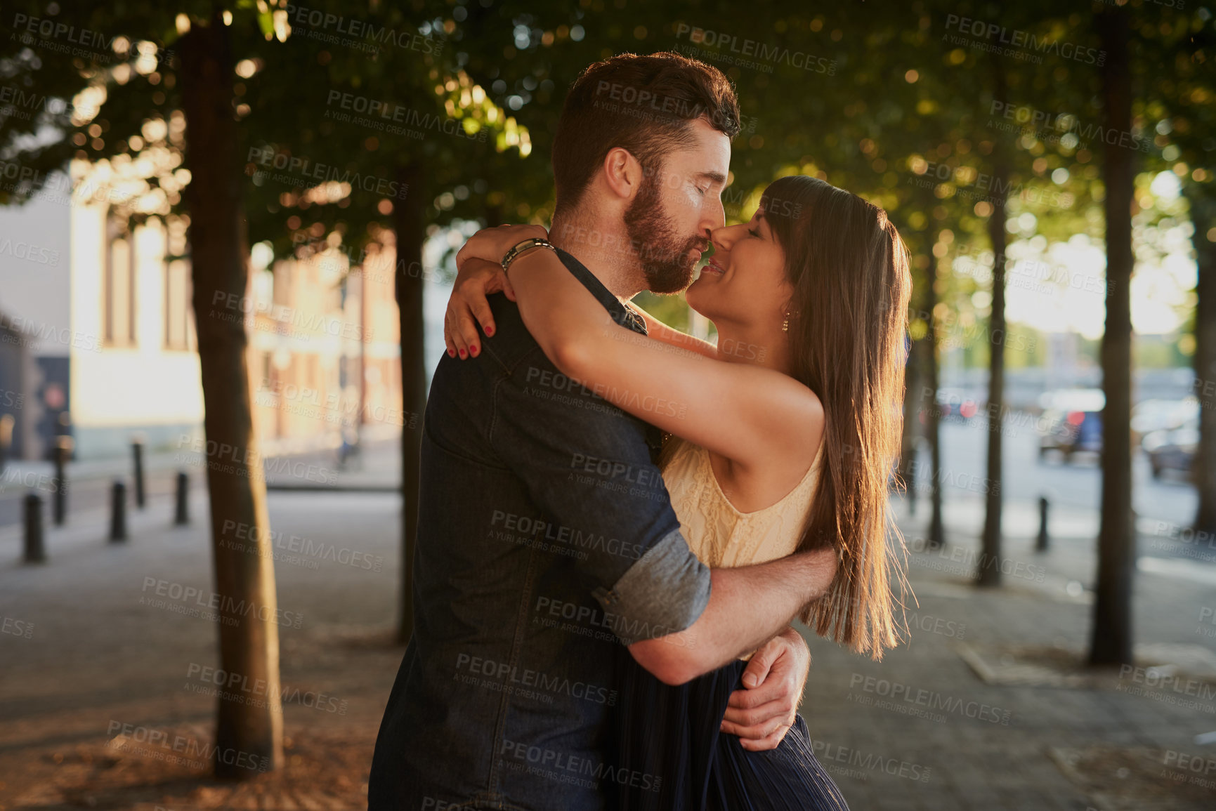 Buy stock photo Kissing, care and couple with hug in nature for romance, connection and happiness together. Love, embracing and young people with bonding for sweet moment, commitment or marriage outdoor in city.