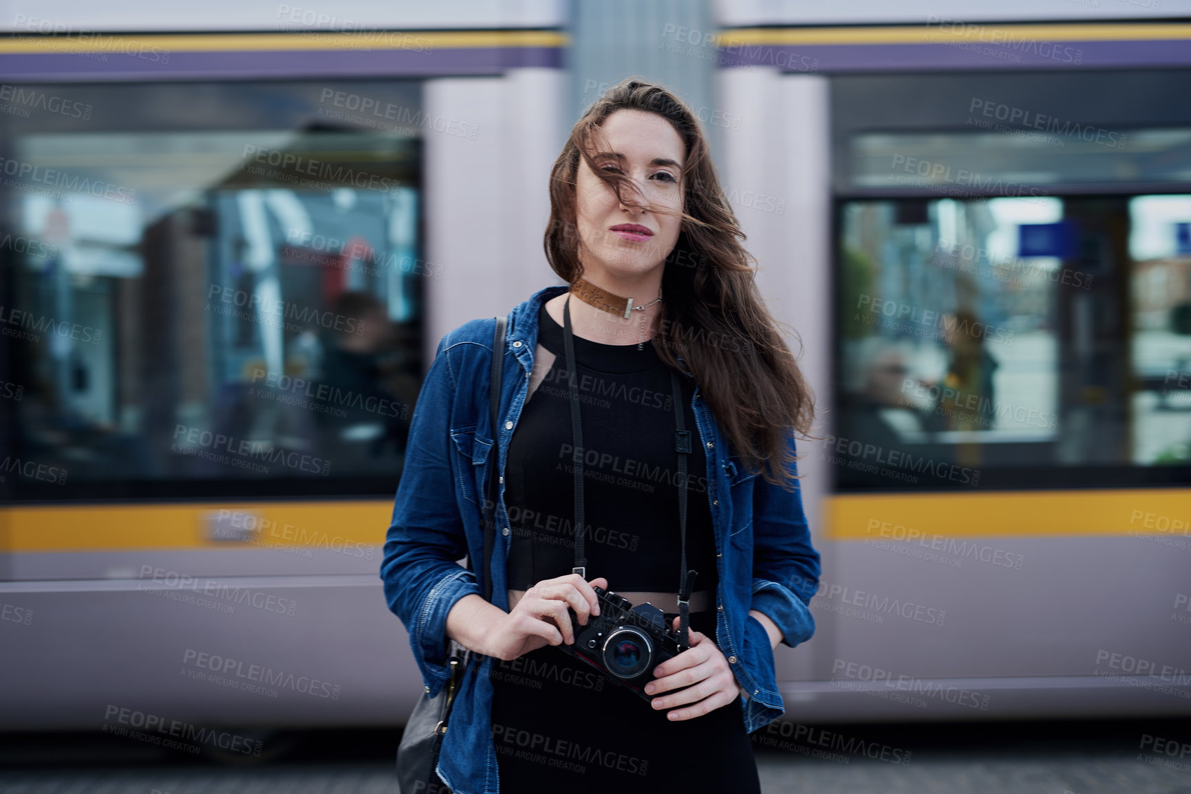 Buy stock photo Portrait of an attractive young female photographer standing on the subway with a train passing through in the background