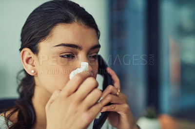 Buy stock photo Shot of a young businesswoman blowing her nose while speaking on a phone in an office