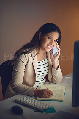 Buy stock photo Shot of a young businesswoman using a mobile phone and writing notes during a late night at work