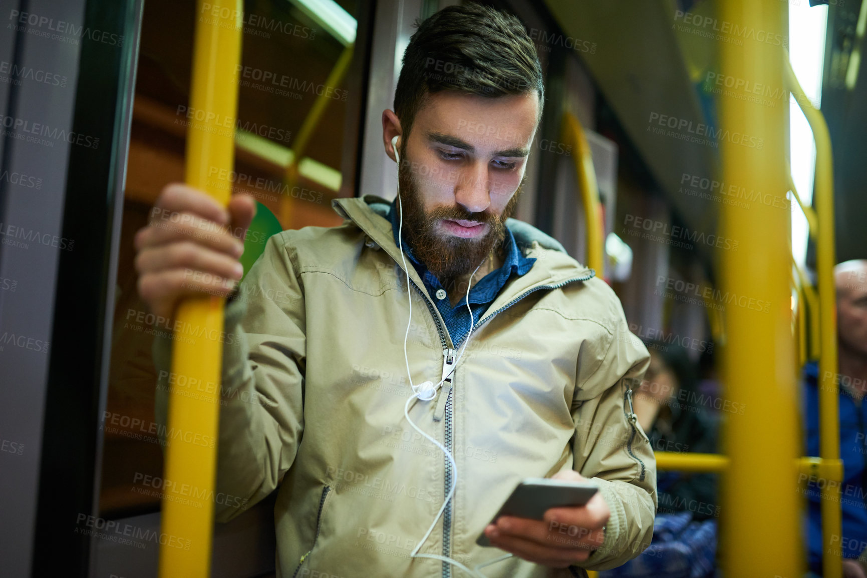 Buy stock photo Cropped shot of a handsome young man listening to music on his cellphone while travelling on a bus