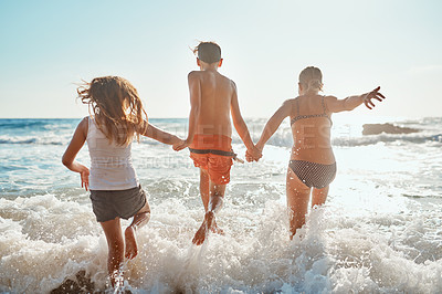 Buy stock photo Shot of siblings running into the water at the beach on a sunny day