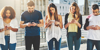 Buy stock photo Cropped shot of a group of young people texting on their cellphones while standing outdoors