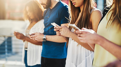 Buy stock photo Cropped shot of a group of unrecognizable young people texting on their cellphones while standing outdoors
